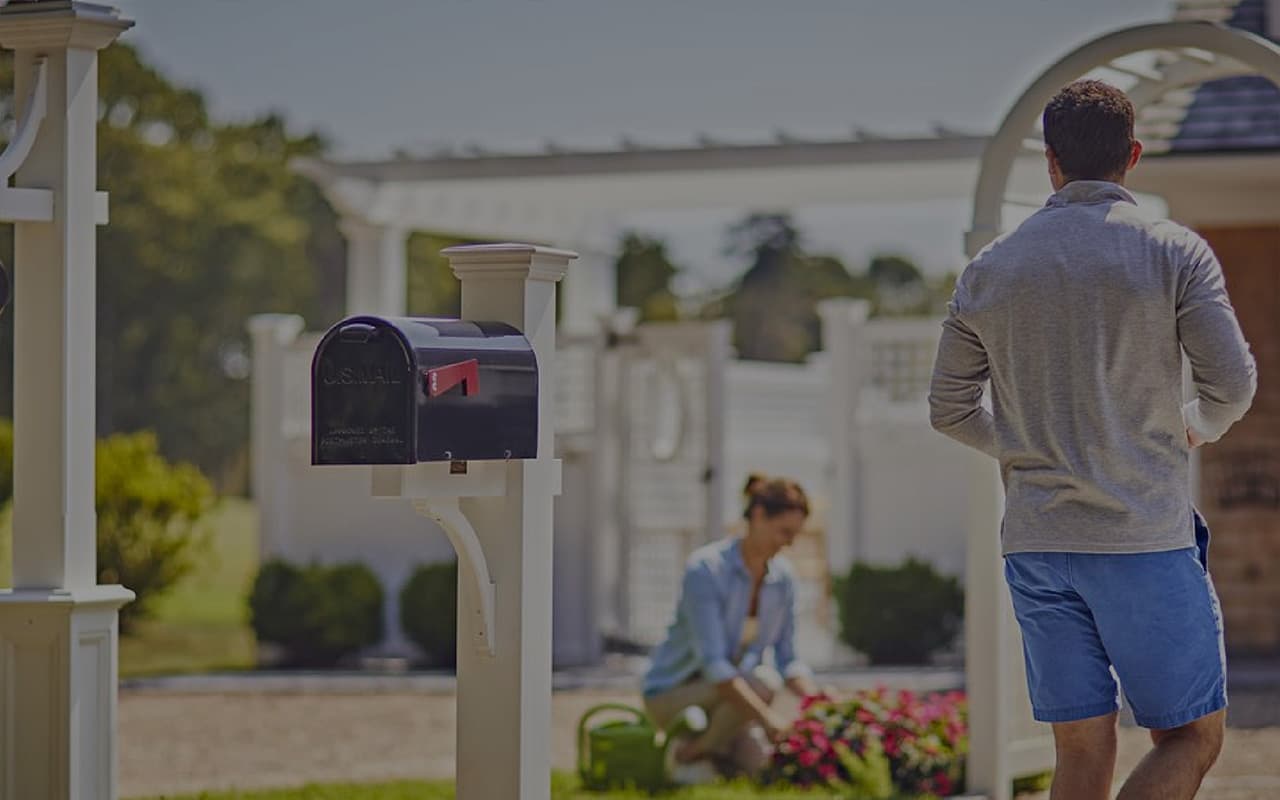 man walking past mailbox towards a woman watering flowers in her yard